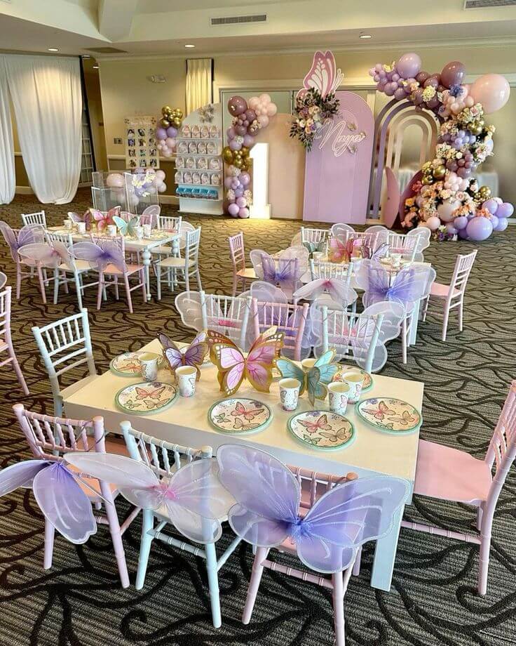Luxury butterfly theme birthday decoration with pastel balloon arch, customized kids seating and elegant party setup