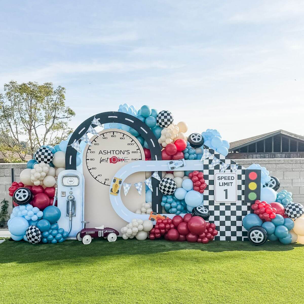 Racing car theme first birthday decoration with balloon arch, speed track backdrop and customized kids birthday setup