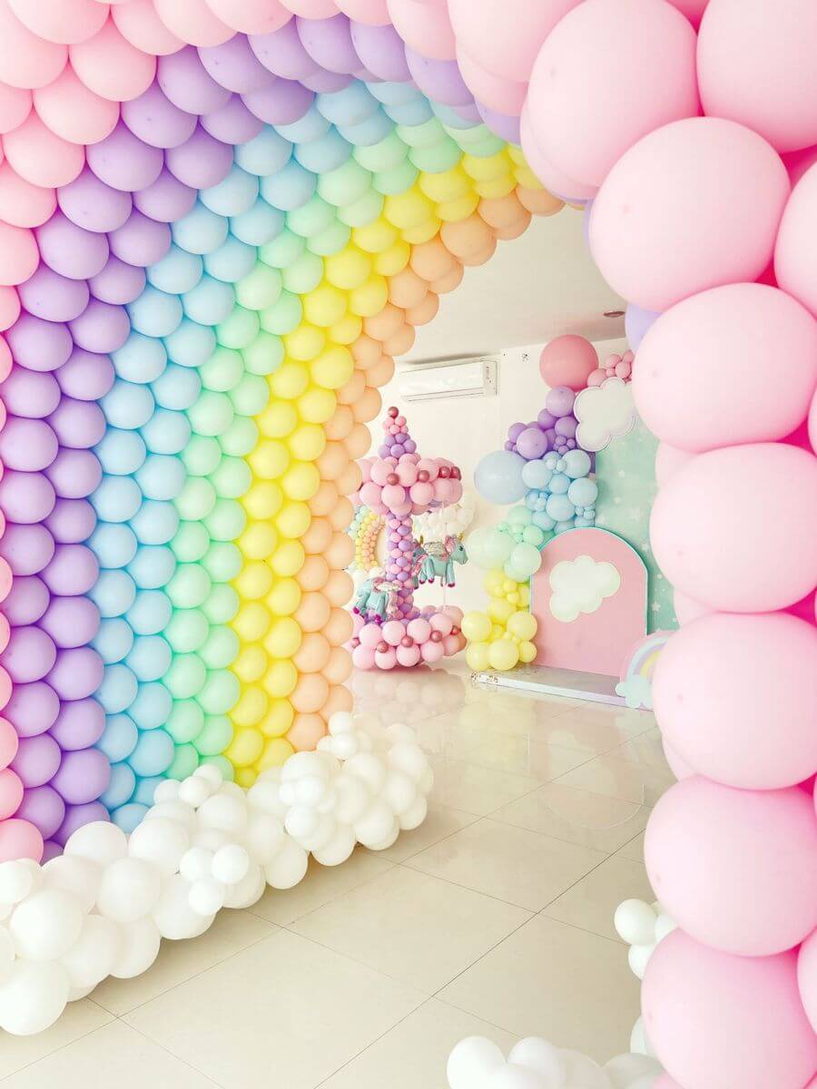 Rainbow pastel balloon arch birthday decoration with unicorn carousel setup and premium kids party backdrop