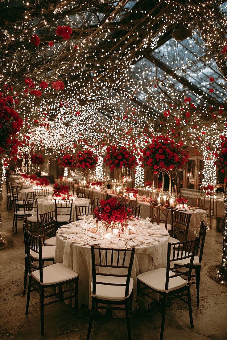 Luxury wedding reception dining area with candlelight tables, red rose centerpieces and fairy light ceiling decor