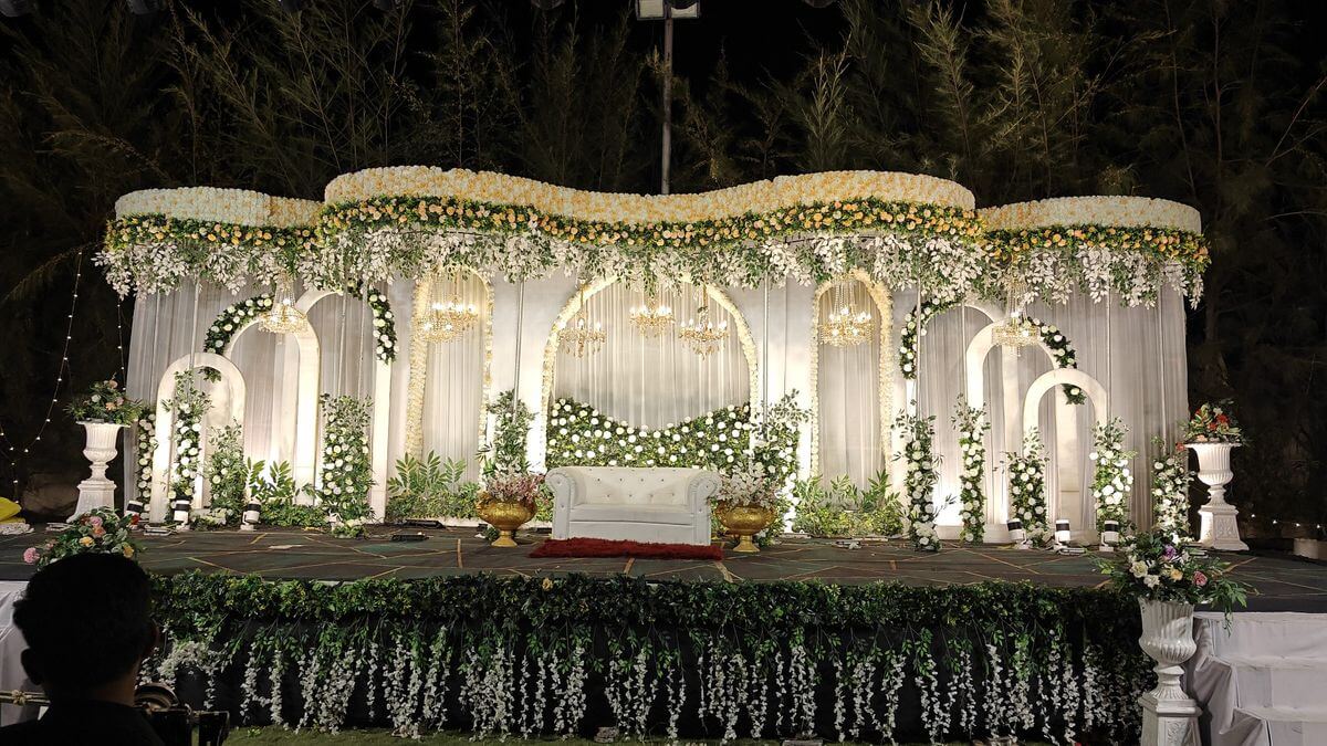 Luxury white floral wedding reception stage decoration with arches, chandeliers and elegant seating